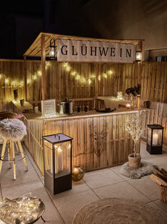 an outdoor bar is lit up with candles and lights on the outside, along with stools