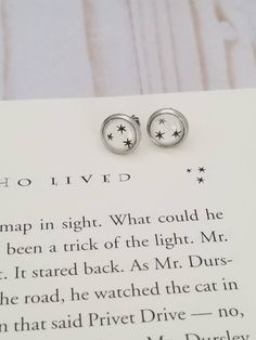 two silver earrings sitting on top of a piece of paper next to an open book