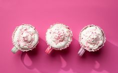 three cupcakes with white frosting and sprinkles on pink background