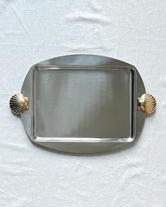 a silver tray with two gold handles on a white tableclothed surface, in the shape of a shell