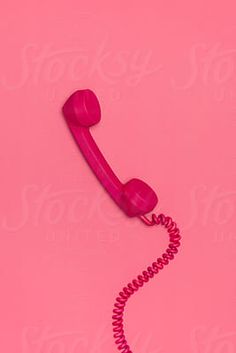 a pink phone on a pink background with the cord still attached to it's receiver