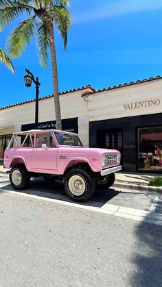 an old pink truck parked in front of a building with a palm tree on the sidewalk