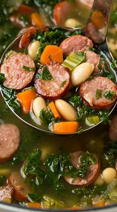 a ladle full of soup with sausage, beans and kale in the bowl