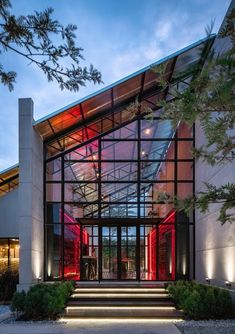 the entrance to a modern building lit up with red lights and plants on either side