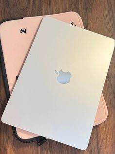 two apple laptops sitting on top of each other in front of a wooden table