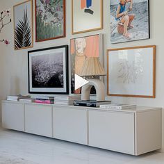 a white entertainment center with pictures on the wall above it and a lamp next to it