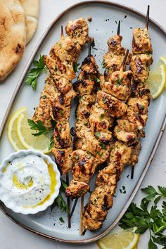 grilled chicken skewers with lemon wedges and sour cream sauce on a platter