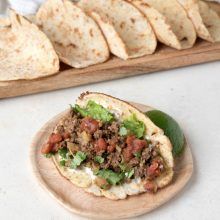 a tortilla with meat and vegetables is on a wooden plate next to some tortillas