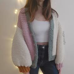 a woman standing in front of a white wall wearing a pink and grey knitted jacket