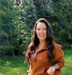 a woman standing in the grass with her hand on her hip and smiling at the camera