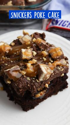 a white plate topped with brownies covered in caramel and chocolate frosting next to a bowl of snickkers poke cake