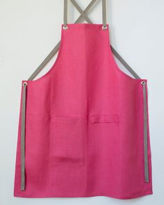 a pink apron hanging on the wall with two metal straps and an open pocket for pockets