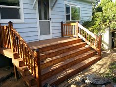 a wooden deck in front of a house with steps leading up to the back door