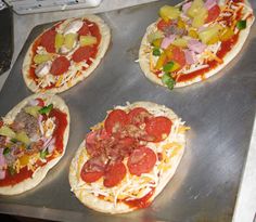 four uncooked pizzas sitting on top of a metal pan covered in toppings