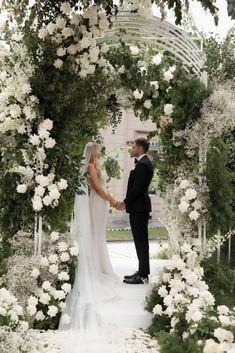 a bride and groom standing under an archway with white flowers