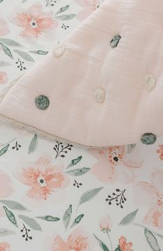 a baby crib with pink and green flowers on it's bedding, next to a wicker basket