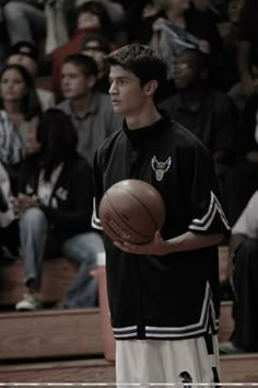 a young man holding a basketball while standing in front of a crowd at a basketball game