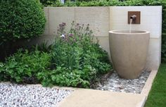 a water fountain in the middle of a garden with rocks and gravel around it, surrounded by greenery