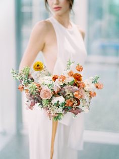 a woman in a white dress holding a large bouquet with orange and pink flowers on it