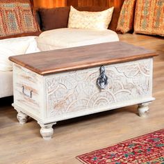 a white trunk sitting on top of a hard wood floor next to pillows and rugs