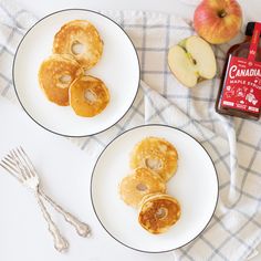 two white plates topped with pancakes next to an apple and maple syrup bottle on a table