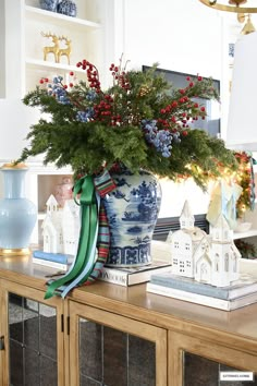 a blue and white vase filled with flowers on top of a wooden table next to a christmas tree