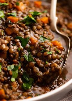 a bowl filled with lentils and carrots on top of a table next to a spoon