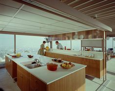 two people are standing at the kitchen counter looking out over the city from an open floor plan