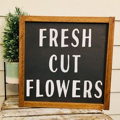 a sign that says fresh cut flowers in white lettering on a wooden frame next to a potted plant