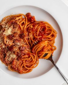 spaghetti with sauce and parmesan cheese on a white plate next to a fork