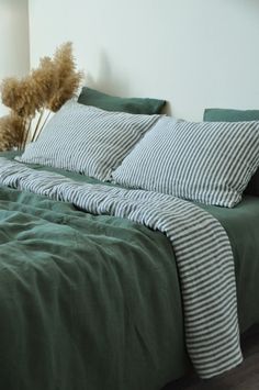 a bed with green sheets and pillows on top of it next to a plant in a vase