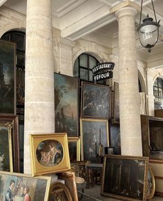 there are many paintings on display in this room with columns and lights hanging from the ceiling