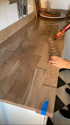 a person that is laying some kind of tile on the counter top with their hand