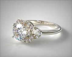 an engagement ring with a flower design on the side and round brilliant cut diamond in the center