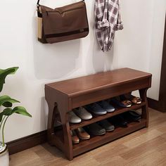 a wooden bench with shoes on it next to a plant and purse hanging from the wall