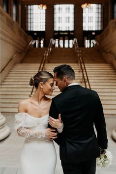 a bride and groom standing in front of stairs