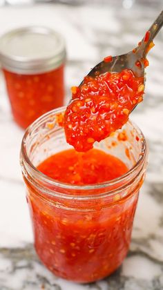 a spoon full of ketchup sitting on top of a jar filled with sauce