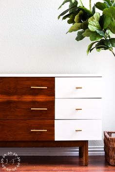 a white and brown dresser sitting on top of a wooden floor next to a potted plant