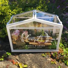 a glass box sitting on top of a rock next to plants and flowers in the background