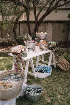 an outdoor party with ice buckets and food on the table in front of some trees