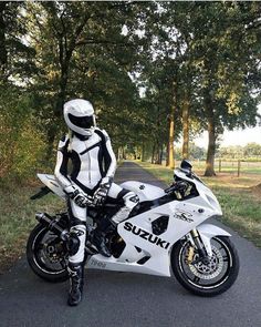 a man dressed in white and black is sitting on a motorbike with trees behind him