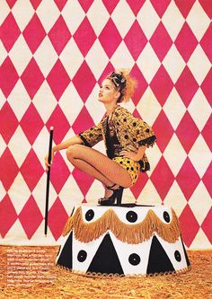 a woman is sitting on top of a circus clown's hat and holding a cane