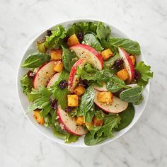 a salad with apples and cranberries in a white bowl on a marble table