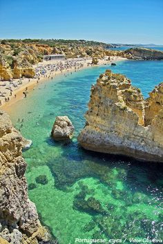 people are swimming in the clear blue water next to rocky cliffs and beach with large rock formations