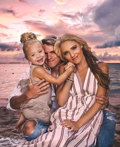 a man, woman and child are sitting on the beach at sunset with their arms around each other