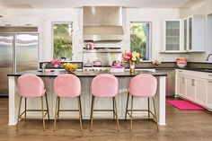 a kitchen with white cabinets and pink chairs next to an island in the middle of the room