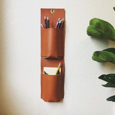 a leather pen holder with pens and pencils in it next to a potted plant