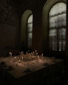 the table is set with candles and place settings in front of two large arched windows