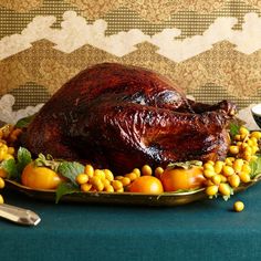 a roasted turkey on a platter with corn, tomatoes and green leaves around it