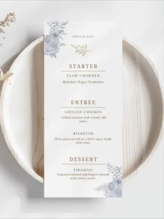 a white and gold wedding menu card on a plate with silver flowers in the center